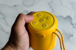 Hand holding a yellow portable speaker with buttons.